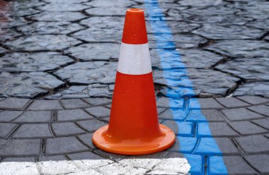 Parlak turuncu yol konisi asfalt yolda duruyor, trafiğe dikkat etmek ve kalabalık bir şehir ortamında güvenliği sağlamak için.