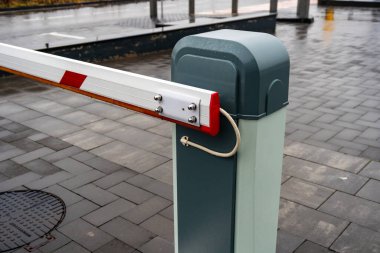 Bir bariyer kapısı bir otoparkın girişinde duruyor. Yağmur asfalta yağarken yansıtıcı bir yüzey oluşturuyor.