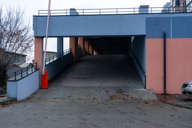 Bir otopark rampası, bulutlu bir günde, kapısı ve dağınık yaprakları olan mavi ve pembe bir yapıya doğru gidiyor.