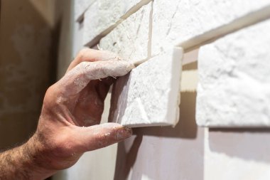 Bir el ustalıkla bir ev geliştirme görevi sırasında duvara taş döşemeleri yerleştirir.