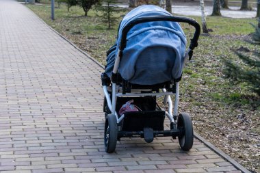 Açık, güneşli bir günde ağaçlarla çevrili sakin bir parktaki tuğla bir yolda bir bebek arabası, açık havada dinlenmeye davet edilir.