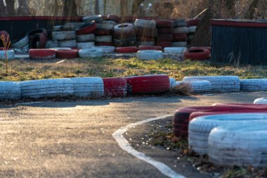Bariyerler olarak eski lastikleri içeren bir go-kart pisti çimenli bir alanda görünür, altın saat ışığıyla aydınlatılır, sessiz bir anı yansıtır.
