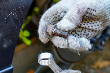 Bir el yeni sökülmüş bir cıvata tutar, diğer elinde İngiliz anahtarı.