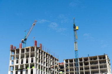 Turnalar, kentsel bir ortamda güneşli bir günde parlak mavi gökyüzüne karşı yeni bir binanın şekillendiği bir inşaat alanında faaliyet gösteriyor.