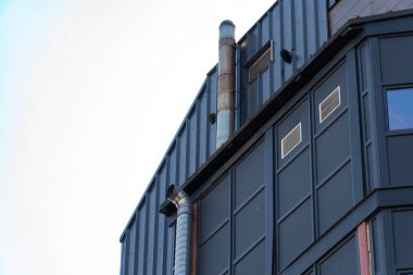 Çarpıcı bir binada, çağdaş mimari eğilimleri vurgulayan, parlak mavi gökyüzüne karşı eşsiz metalik yapılar ve havalandırma boruları yer alıyor.