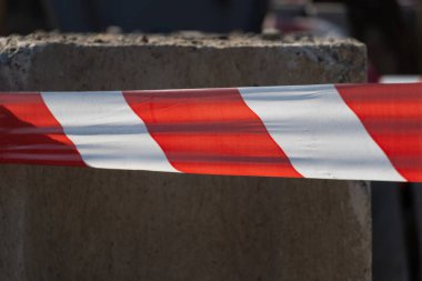 Red and white barrier tape restricts access around a construction site, ensuring safety and caution as work continues in a bustling urban area clipart