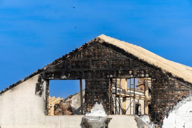 Yanmış bir binanın kalıntıları duvarları yaktı ve gün boyunca arka planda parlak mavi bir gökyüzü olan ahşap iskeleti ortaya çıkardı..