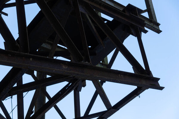 A metal lattice structure looms against a clear blue sky, showcasing its intricate design and signs of rust and age, reflecting industrial beauty and decay