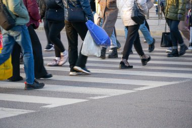 Kalabalık bir şehirde, işaretli yaya şeridini geçen gruplar, akşam trafiğinde yol alırken çantalarını taşıyorlar.