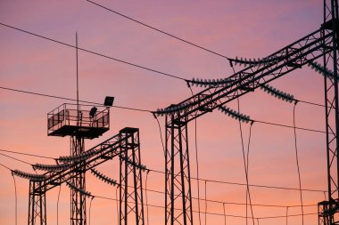 Elektrik kablolarının siluetleri ve elektrik kuleleri renkli bir günbatımına karşı yükseliyor ve günbatımında endüstri ile doğanın karışımını gözler önüne seriyor.
