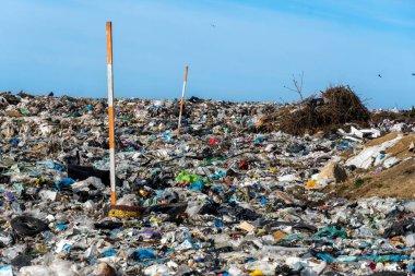 Plastik, enkaz ve mavi gökyüzünün altındaki atıkla dolup taşmış. Çevre kirliliği, ekolojik sorunlar ve atık yönetimi sorunlarını gözler önüne serer.
