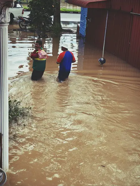 Sel sularında yürüyen iki kişi diğerlerine yardım etmeye çalışıyor..