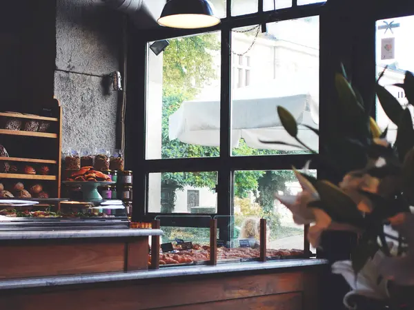 Hamur işleri sergilenen bir kafenin içi sıcak ve sabah ışığı büyük pencerelerden içeri akıyor. Kırsal dekor ve çiçekler davetkar atmosfere eklenir