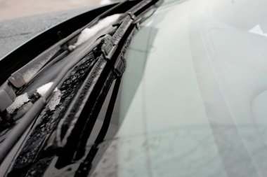 Görünür silecek bıçaklarla kaplı bir arabanın ön camının yakın çekimi, kış havasını ve buzlu koşulları vurguluyor..