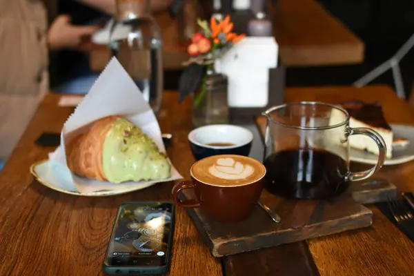 İçinde sanat olan bir latte, bir çaydanlık kahve, tereyağlı kruvasan ve cheesecake bulunan nefis bir kafe. Kahve molası için son derece rahat ve davetkar bir ortam..