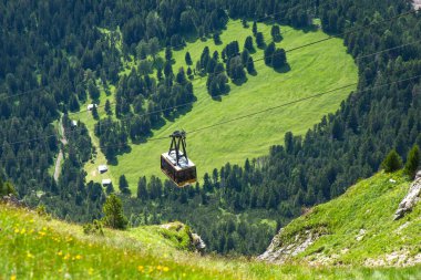 Dolomitler, İtalyan---24 Temmuz 2024: Seceda teleferiği yazın arka planda orman ve çimlerle havada hareket ediyor