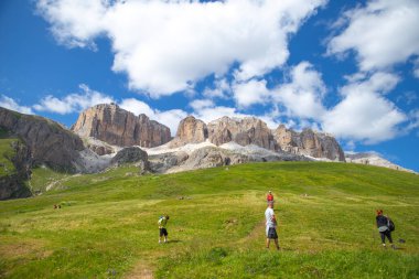 Dolomitler, İtalyan---29 Temmuz 2024: arka planda kayalık dağ ile çimlerin üzerinde güneşin tadını çıkaran turistler