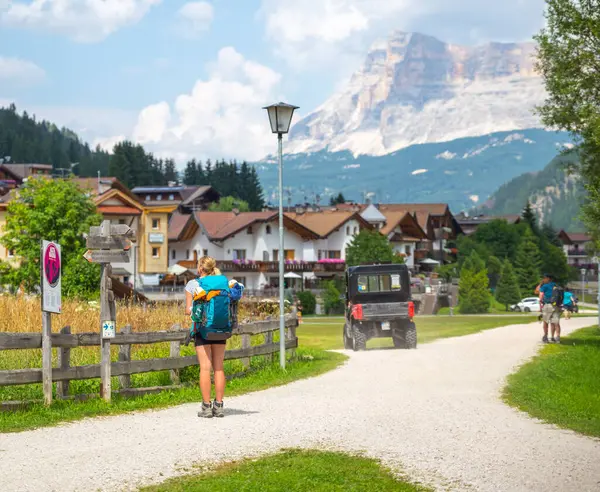 Dolomitler, İtalyan---27 Temmuz 2024: Büyük bir sırt çantası taşıyan sarışın bir kız yazın Corvara 'da yol işaretlerine bakıyor.