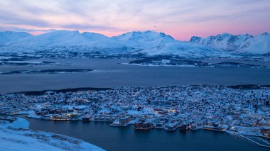 Norveç 'in Utsiktspunkt şehrinin kutup gecesinde ışıklarla, kar dağlarıyla ve pembe gökyüzüyle göz önüne alındığında