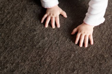 Halılı zeminde sürünürken bir bebeğin ellerini yakın plan çek.