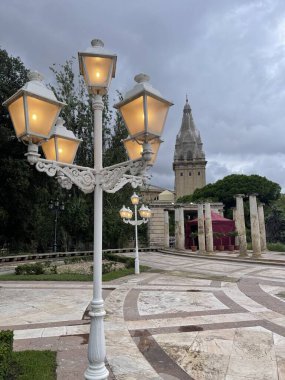 A vintage streetlight on a pole stands gracefully in a Barcelona park, its intricate design adding a touch of old-world charm amid lush greenery, blending history with nature. clipart