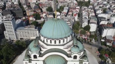 Sırbistan 'ın Belgrad kentindeki Saint Sava Katedrali' nin parklarla çevrili beyaz mermer, yeşil kubbeler ve altın haçlarla ve çağdaş ve tarihi mimariyle harmanlanmış bir şehir manzarasıyla çarpıcı bir hava manzarası..