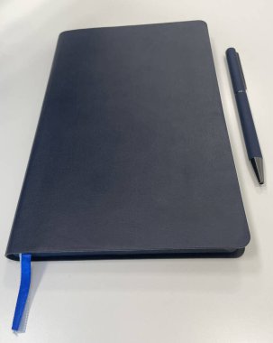 Minimalistic composition featuring a sleek navy blue notebook with a blue ribbon bookmark, placed on a clean white surface.  clipart