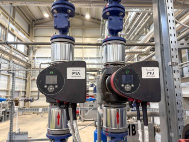 Etiketli kontrol panelleri ve paslanmaz çelik borular, otomasyon, tesisat veya enerji sistemleri için kullanılan modern bir tesisin içindeki endüstriyel su pompa sistemi..