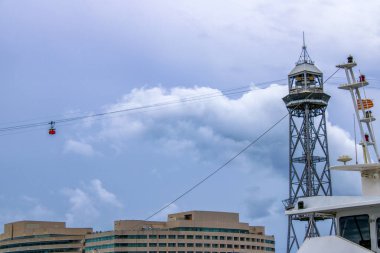 Barcelona 'da hareket halindeki kentsel teleferik sisteminin çarpıcı bir görüntüsü. Kablolarda asılı duran parlak kırmızı bir gondol dramatik bulutlu gökyüzüne karşı..