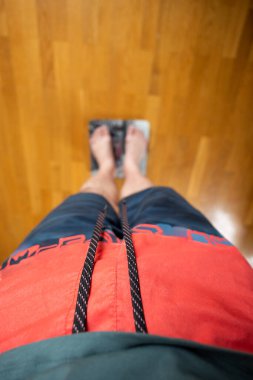 Kabartmalı ahşap bir zeminde kırmızı ve mavi atletik şort giyen bir adamın görüntüsü. Fitness, sağlık takibi ve kişisel sağlık bu samimi ve anlaşılabilir fotoğrafın ana teması. Seçici odak