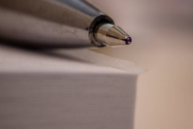 Tükenmez kalemin ucu bir yığın beyaz kağıdın üzerinde duran yakın çekim makro görüntüsü. Görüntü, kalemin hassasiyetini ve kağıdın dokusunu yakalar, detaylara, işçiliğe ve yazma araçlarına vurgu yapar.