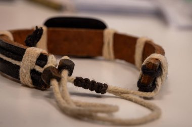 Beyaz bir yüzeye örülmüş, el yapımı deri bir bileziğin yakın çekimi. Moda aksesuarları, zanaatkar ürünleri ya da bohem tarzı temalar için ideal malzemelerin kırsal işçiliği ve doğal dokusu
