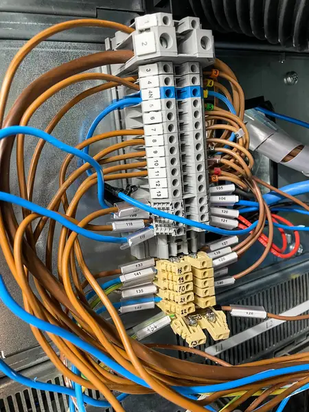 Endüstriyel bağlantı kutusunun içindeki, detaylı bir elektrik terminali bloğunun yakın çekimi. Görüntü, elektrik mühendisliği ve otomasyon sistemlerinin hassasiyetini ve organizasyonunu yakalayan karmaşık bir renk kodlu kablo dizisini ve numaralandırılmış terminalleri gösteriyor.