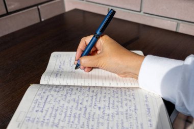 Bir kişinin el yazısının dolmakalemle planlayıcıyla yakın plan görüntüsü. Arkaplanda ahşap bir masa ve seramik bir duvar var. Sakin ve verimli bir ortam yaratıyor.