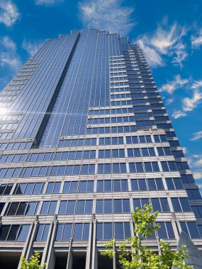 Parlak mavi gökyüzü ve ince bulutlar üzerinde yansıtıcı cam paneller olan modern bir gökdelenin alçak açılı görüntüsü. Bir metropol ortamında şehir mimarisi ve iş konsepti.