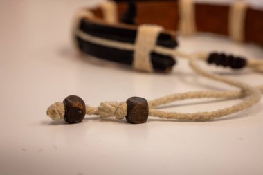 Üzerinde krem rengi sicim, koyu ahşap boncuklar ve deri elementler bulunan el yapımı bir bileziğin yakın çekim makro görüntüsü..