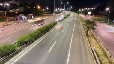 Kırmızı ve beyaz araba ışıkları çizgilerinin çerçeve boyunca parlak izler çizdiği hareketli bir otoyolun büyüleyici bir gece zaman çizelgesi. Trafiğin hipnotik akışının gelişmiş perspektifi. 