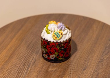Güzel dekore edilmiş geleneksel paskalya pastası, krema ve pastel malzemelerle sade ahşap bir masada duruyor. 