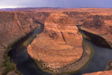 Arizona 'daki Horseshoe Bend' in çarpıcı manzarası, Colorado Nehri 'nin dramatik gökyüzü altında devasa kırmızı uçurumlar etrafında kıvrılıp nefes kesici bir doğal manzara yarattığı yer..