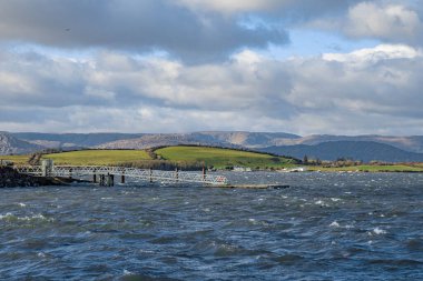 Waves splash against a metal jetty in sunny weather in Bantry, Ireland clipart