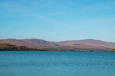 Yeşil adanın olduğu sakin deniz yüzeyi ve İrlanda 'nın arka planında dağlar