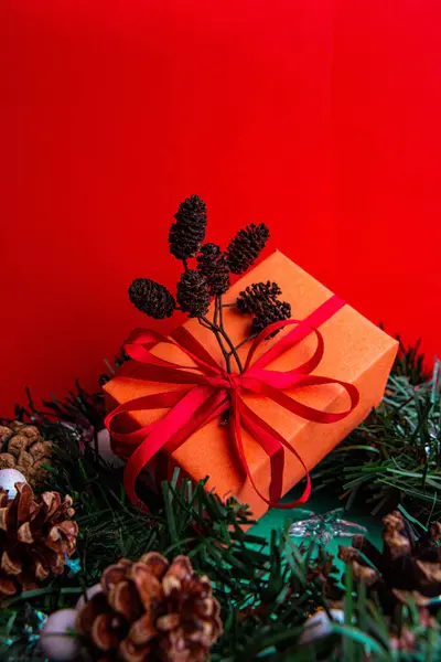 Kırmızı arka planda dekoratif dalı olan turuncu ambalajlı Noel hediyesi