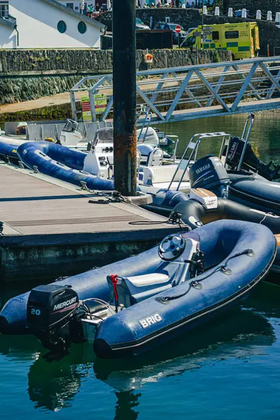 Rıhtımda duran mavi şişme bir teknenin dikey görüntüsü. Çerçevenin üstünde bir iskele var.