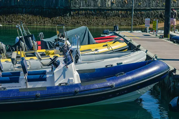 Rıhtımda çok renkli tekneler demirli, ön planda mavi şişme bir tekne var.