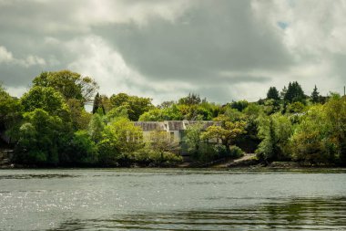 Nehir kıyısındaki bir tekneden ve Glengarriff, İrlanda 'da yeşil ağaçlarda gizlenmiş bir evden görüntüler.