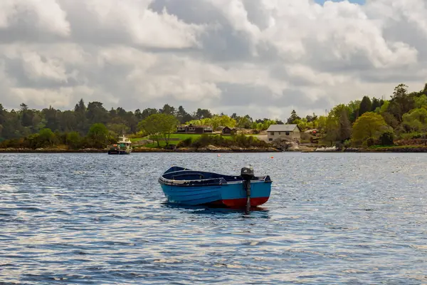  Boş mavi tekne nehir kıyısında, arka planda evleri olan kayalık kıyılarda oturuyor. Batı Cork bölgesinde, Glengarriff, İrlanda