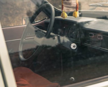 Siyah direksiyonu, kahverengi koltuğu ve hız göstergesi ve diğer kontrolleri olan klasik bir arabanın içi..
