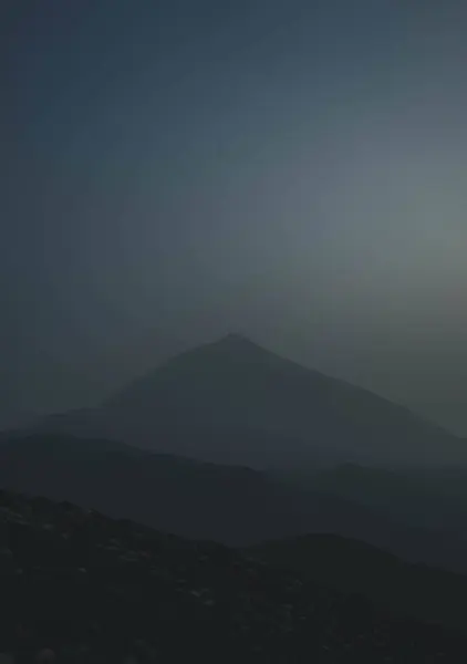 Gün batımında sisle kaplanmış sakin ve gizemli bir dağ manzarası. Engebeli arazi ve puslu atmosfer korku ve sükuneti çağrıştırıyor..