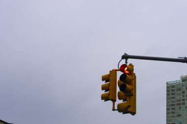 Kırmızı ışıklı bir trafik ışığı, metal bir direkten asılı bulutlu bir gökyüzü ve yüksek bir binanın arka planına karşı..