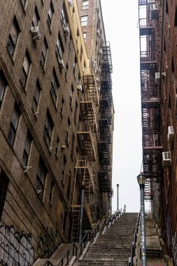 İki eski tuğla bina arasında dar bir merdiven var. Yangın merdivenleri ve duvarlarında grafiti var. Binalar şehir ortamında gibi görünüyor..